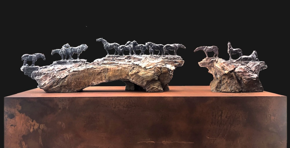 Bronze sculpture of twelve horses across two rocks on a pedestal by Stephanie Revennaugh